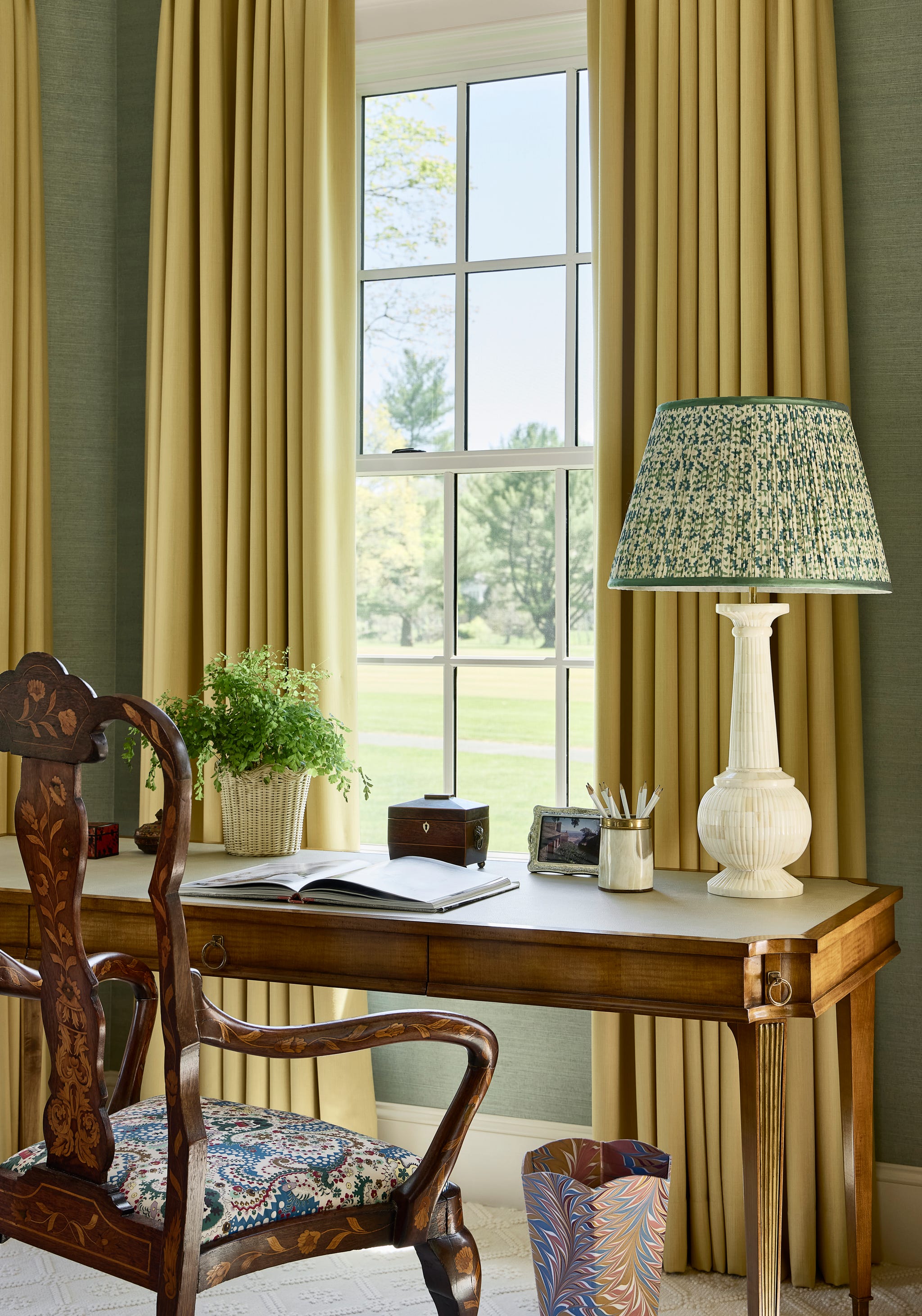 antique desk and chair in front of gold curtains on a window
