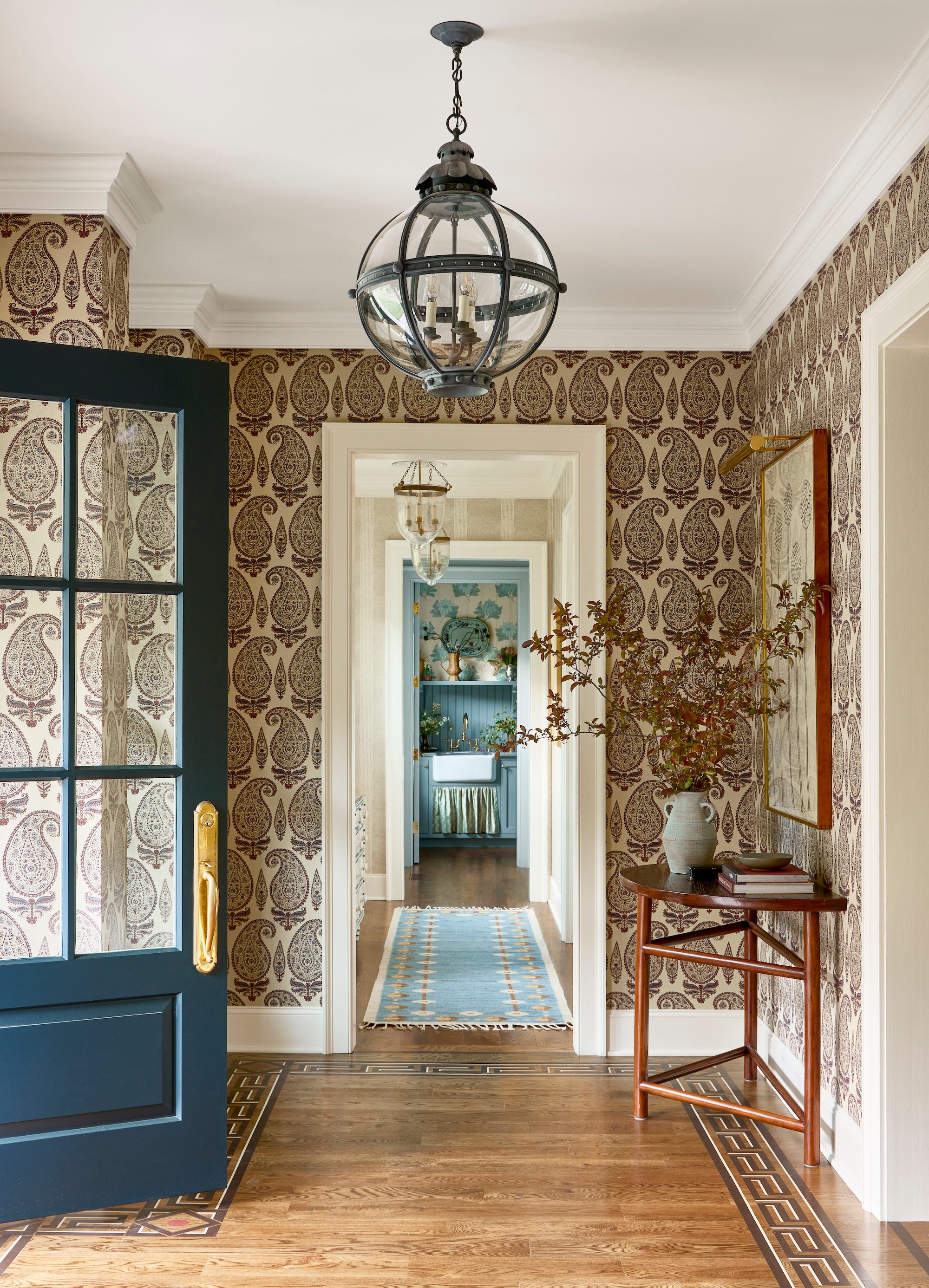 entry with patterned wallpaper, wooden table against the wall, blue door, and lantern on ceiling