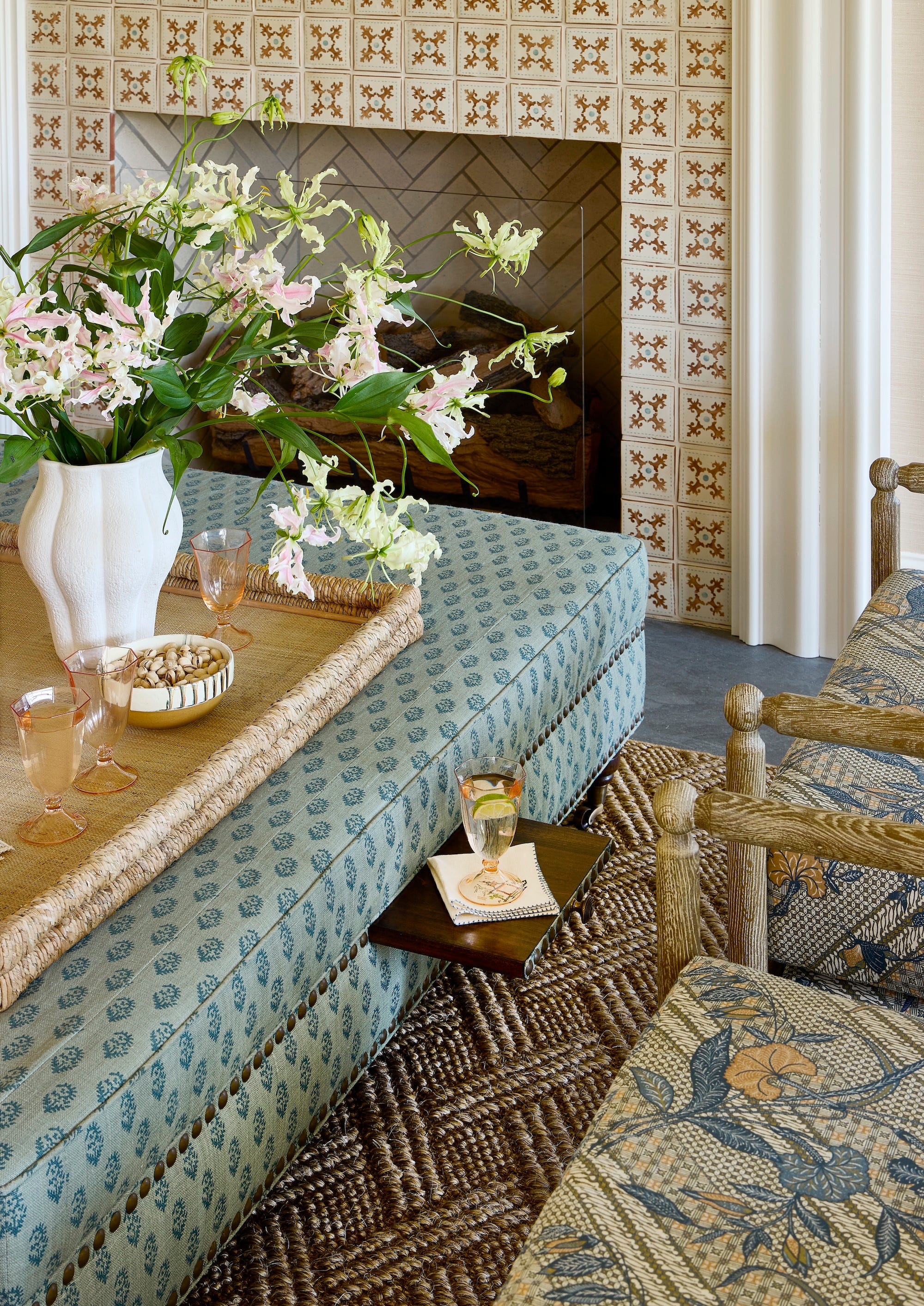 patterned ottoman with a tray on top of it and a fireplace behind it and two chairs next to it