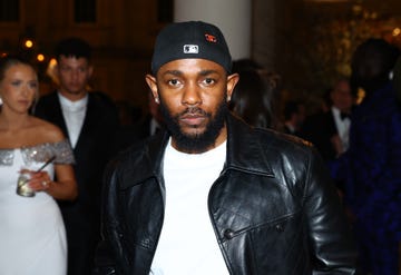 kendrick lamar looks at the camera, he wears a white tshirt, black leather jacket, and backward baseball cap