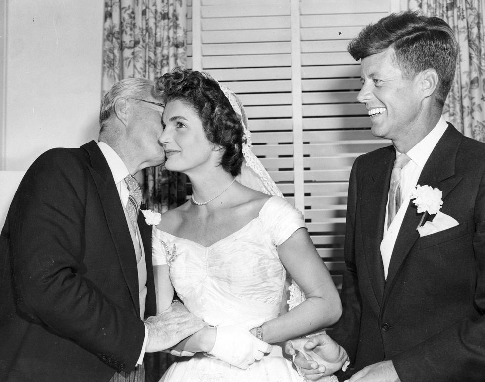 John F. Kennedy smiles as his father, Joseph P. Kennedy Sr., kisses Jackie Kennedy at the couple's wedding reception.