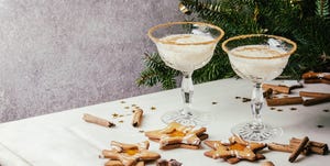 Eggnog Christmas milk cocktail, served in two vintage crystal glasses with shortbread star shape sugar cookies, cinnamon sticks, fir branch over white marble table.