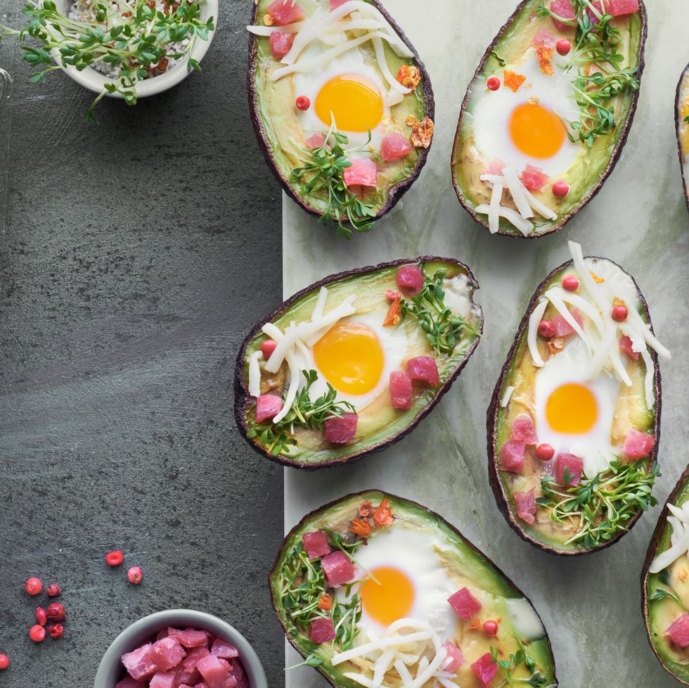 keto diet dish avocado boats with ham cubes, quail eggs, cheese and cress sprouts on stone serving board