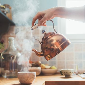 hand holding copper kettle and pouring steaming water into a bowl