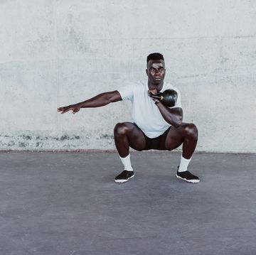 sportsman with arms outstretched holding kettle bell while crouching against wall