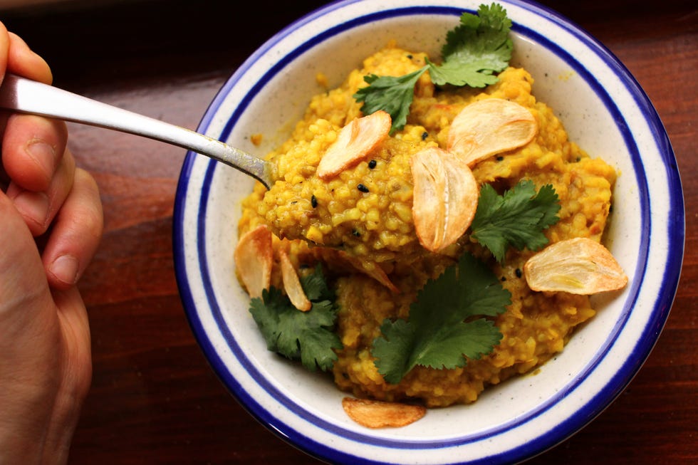 a bowl of turmeric yellow khichdi in a blue rimmed bowl with fried garlic chips and green cilantro