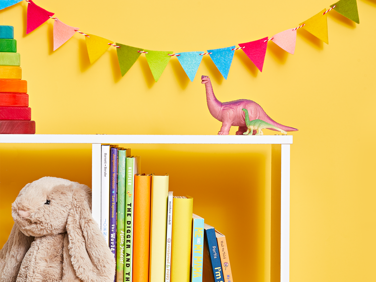 white bookshelf on yellow background with childrens books and a stuffed rabbit and toys