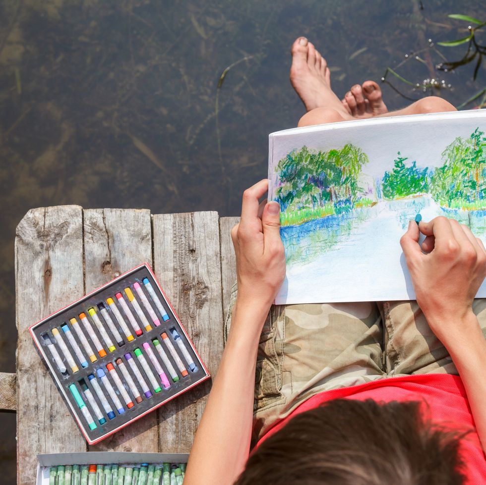 kid drawing a summer landscape with a forest lake as a camping activity