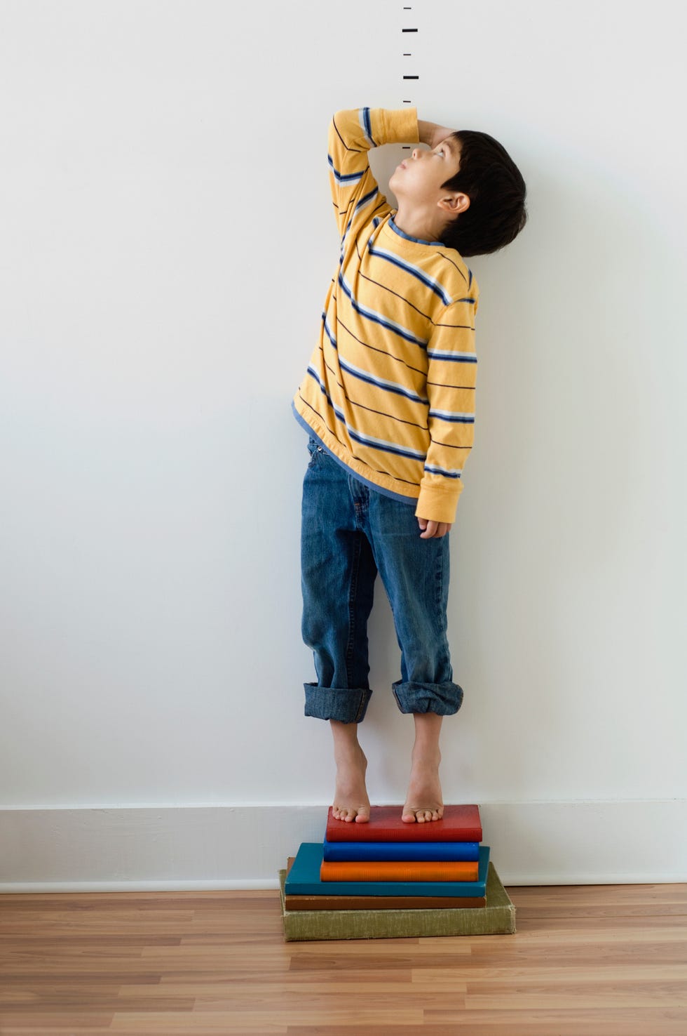 boy standing on books in front of height markers
