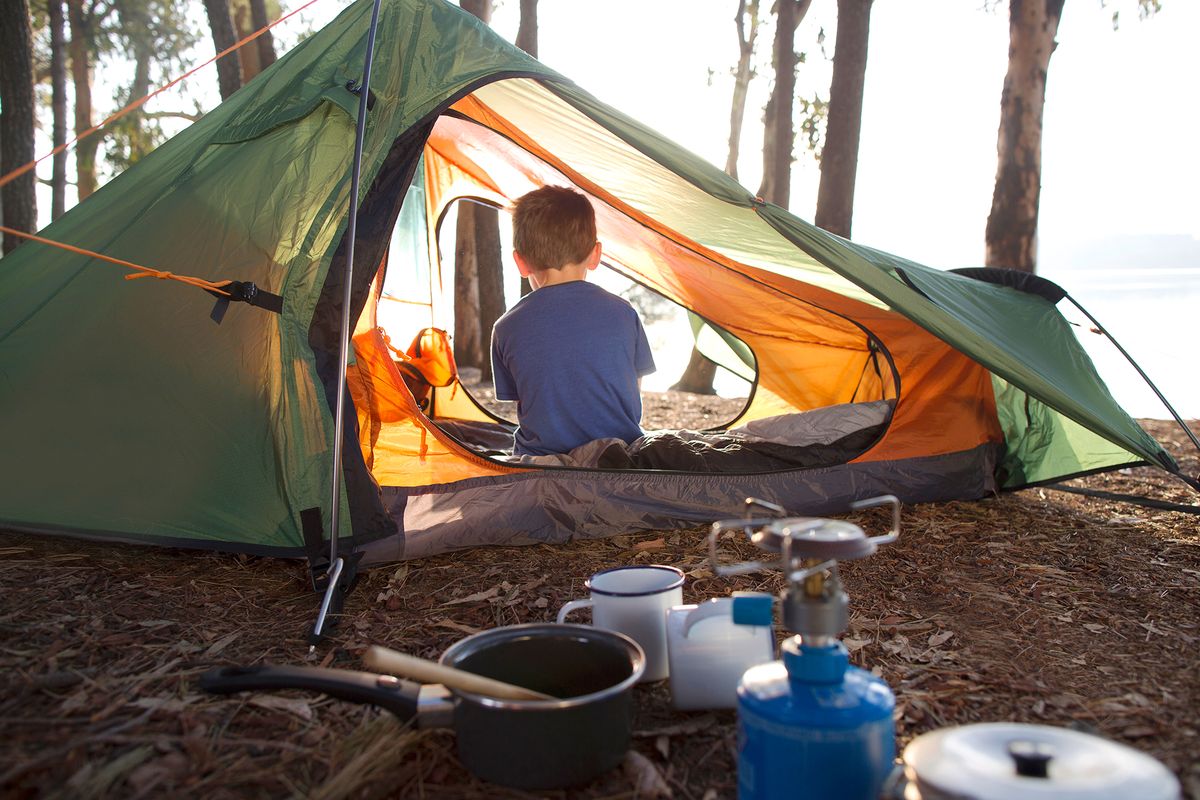 kid sitting in tent with camping supplies