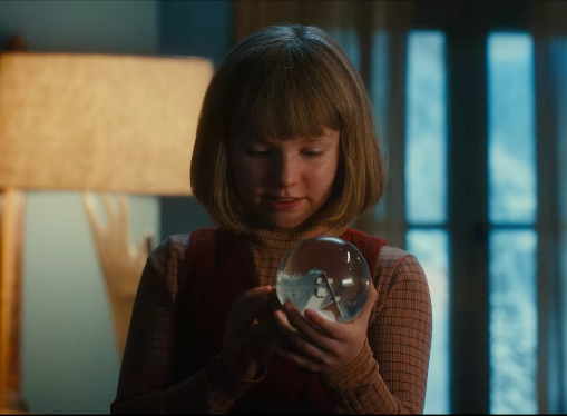 a young girl looks at a snow globe in a scene from the claus family 3