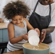 young girl pouring flour into a mixing bowl with mom helping
