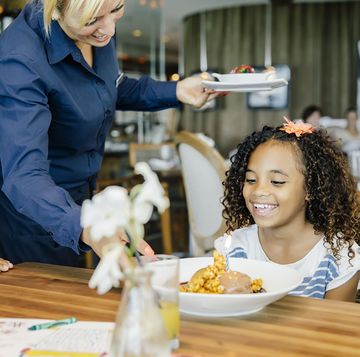girl with flower in her hair smiles as waitress serves her meal in restaurant
