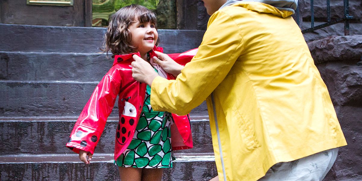 parent in yellow rain jacket putting ladybug rain coat on young child
