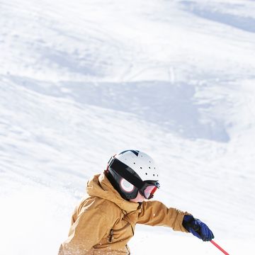 kid skiing down hill with helmet goggles and blue gloves on