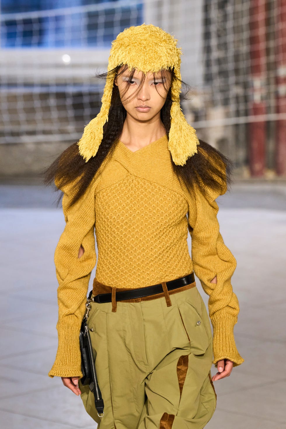 model walking on a runway wearing a yellow knitted sweater and khaki pants