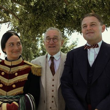 lily gladstone, robert de niro, and leonardo dicaprio in character for killers of the flower moon, they stand together outside underneath greenery and smile