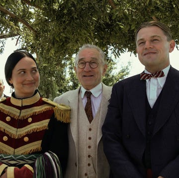 lily gladstone, robert de niro, and leonardo dicaprio in character for killers of the flower moon, they stand together outside underneath greenery and smile