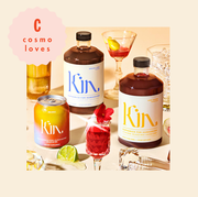This is an image tablescape of non alcoholic cocktails made from kin euphorics, shown in glasses, bottles and cans on a peach background with a variety of fruit with a cosmo loves logo