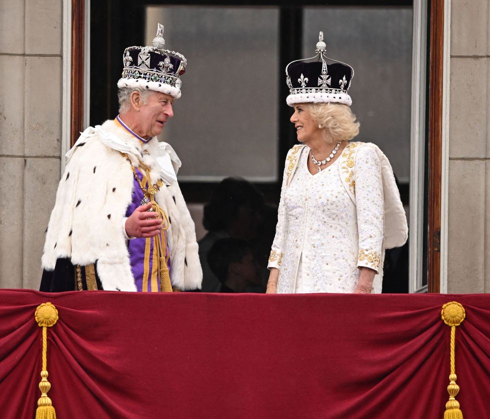 king charles and queen camilla look lovingly at one another on the palace balcony whilst greeting crowds below at the coronation