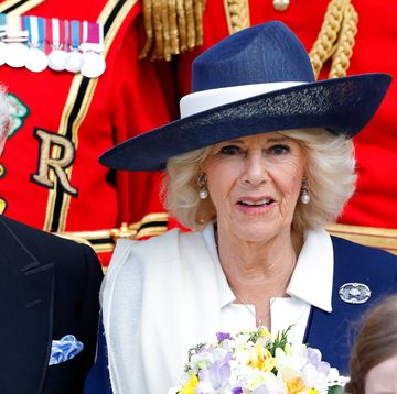 king charles iii, wearing a black suit and blue tie, and camilla, queen consort, wearing a white and blue outfit and blue hat, looking directly ahead