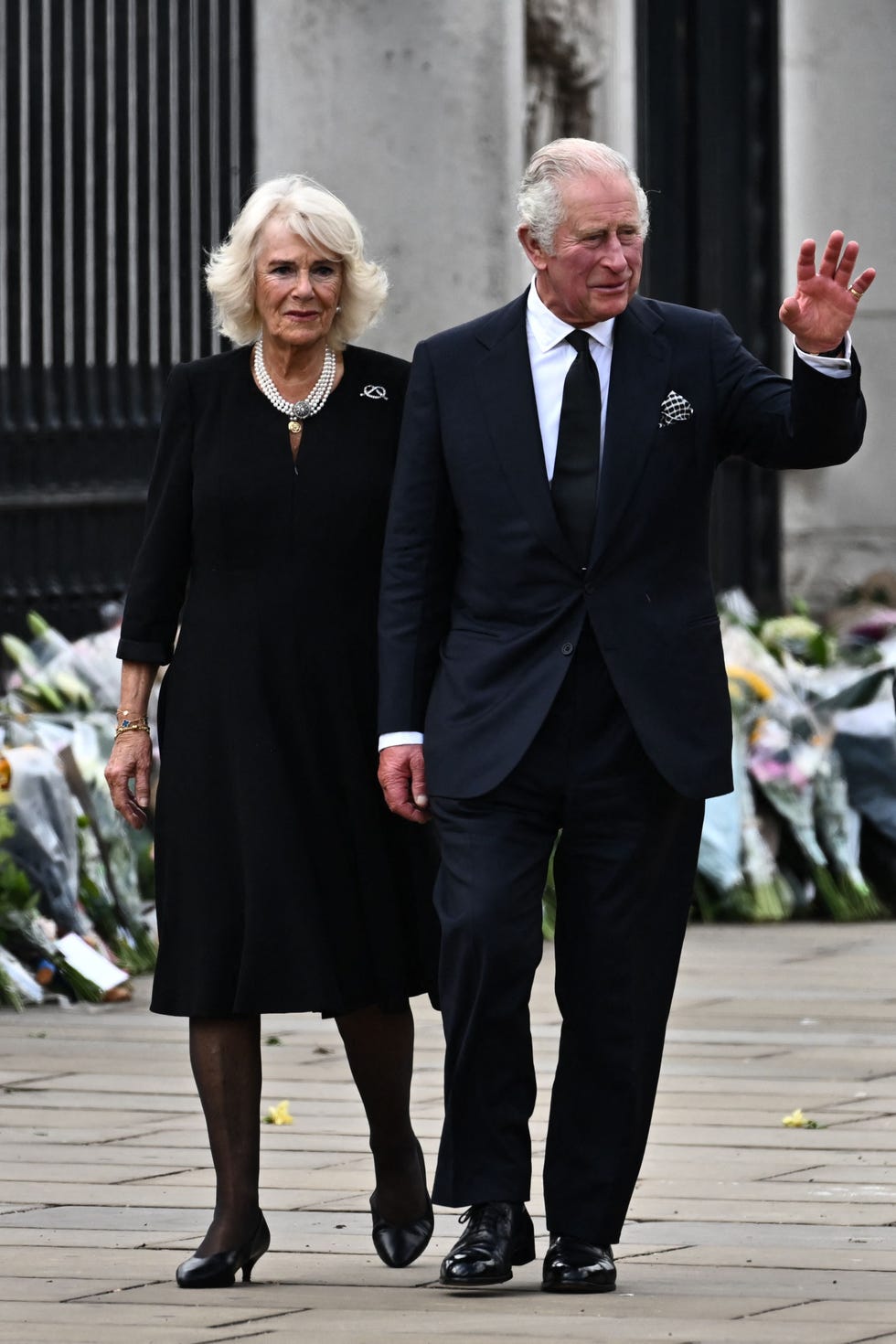 queen consort camilla and king charles iii arrive at buckingham palace, with floral tributes to queen elizabeth ii in the background