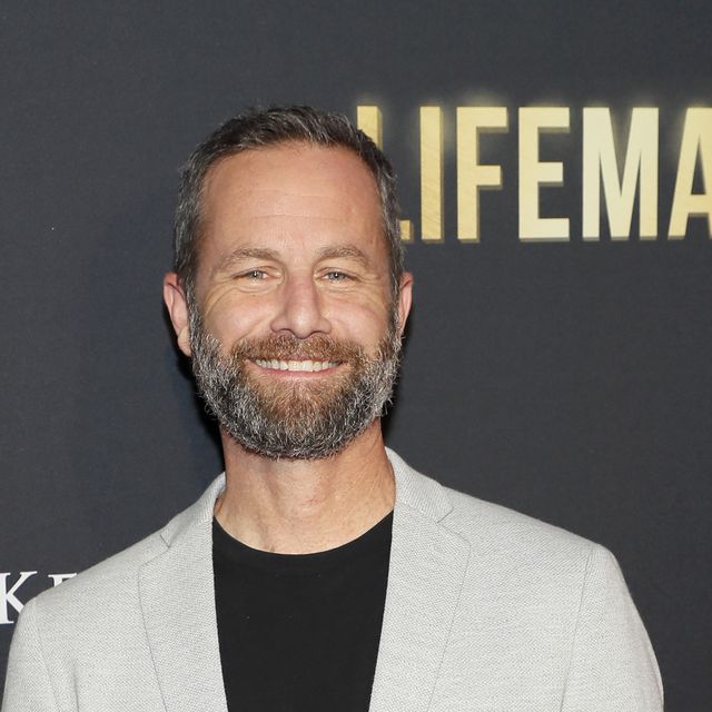 kirk cameron smiles at the camera, he is wearing a light grey suit jacket and a black t shirt, he has a full beard and his hair is short