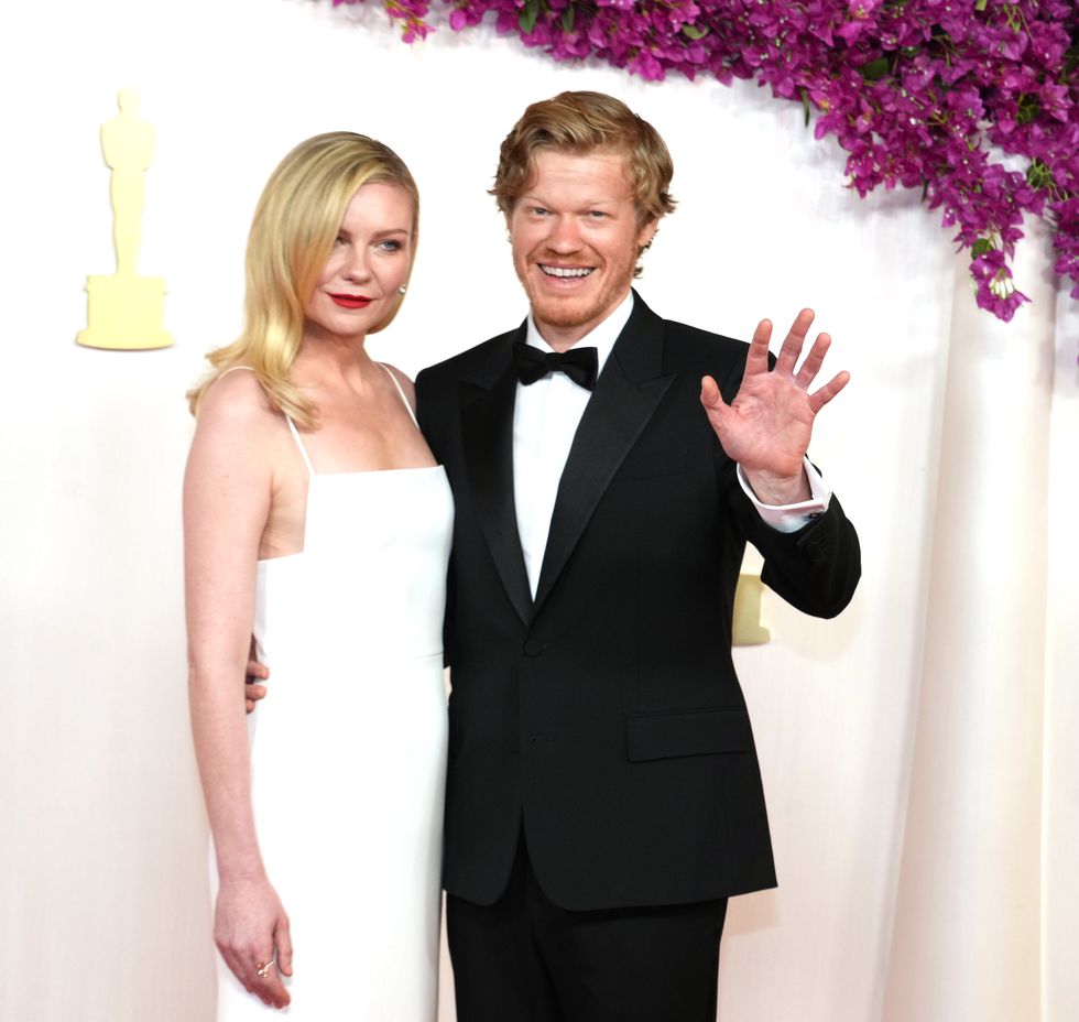 actor jesse plemons waving toward the camera and smiling as he embraces wife kirsten dunst