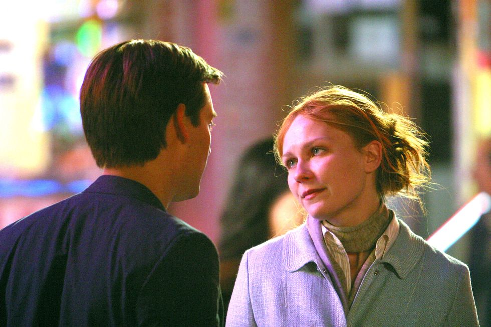 kirsten dunst looks on tobey maguire who faces away from the camera, she wears a coat, collared shirt and scarf