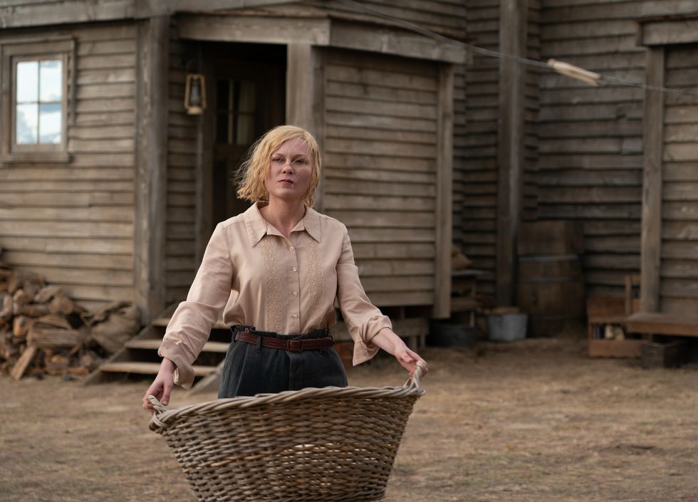 kirsten dunst holding a basket as she walks in front of a house in a scene from a movie