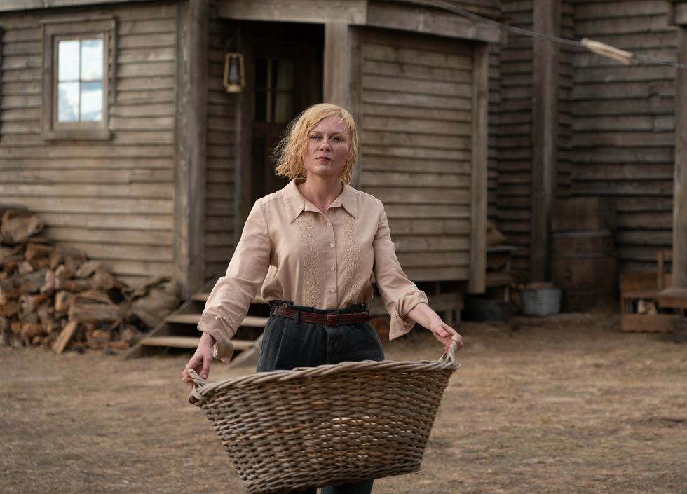 kirsten dunst holding a basket as she walks in front of a house in a scene from a movie