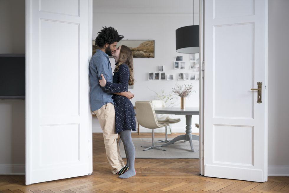 Kissing couple at home standing in door frame in living room