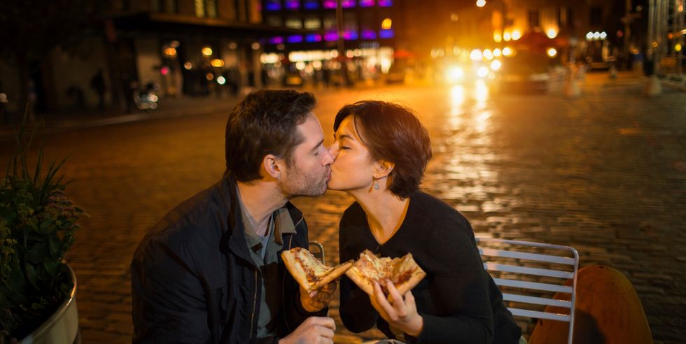kissing couple having pizza outdoors