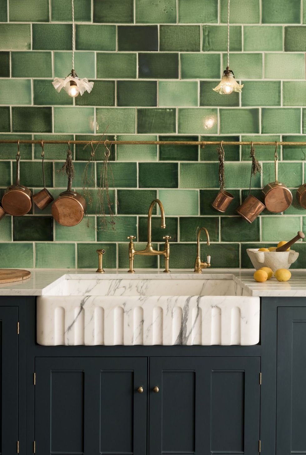 copper pots hung on pot rail in place of upper kitchen cabinets on green tile wall, above butler's sink, dark gray cabinets