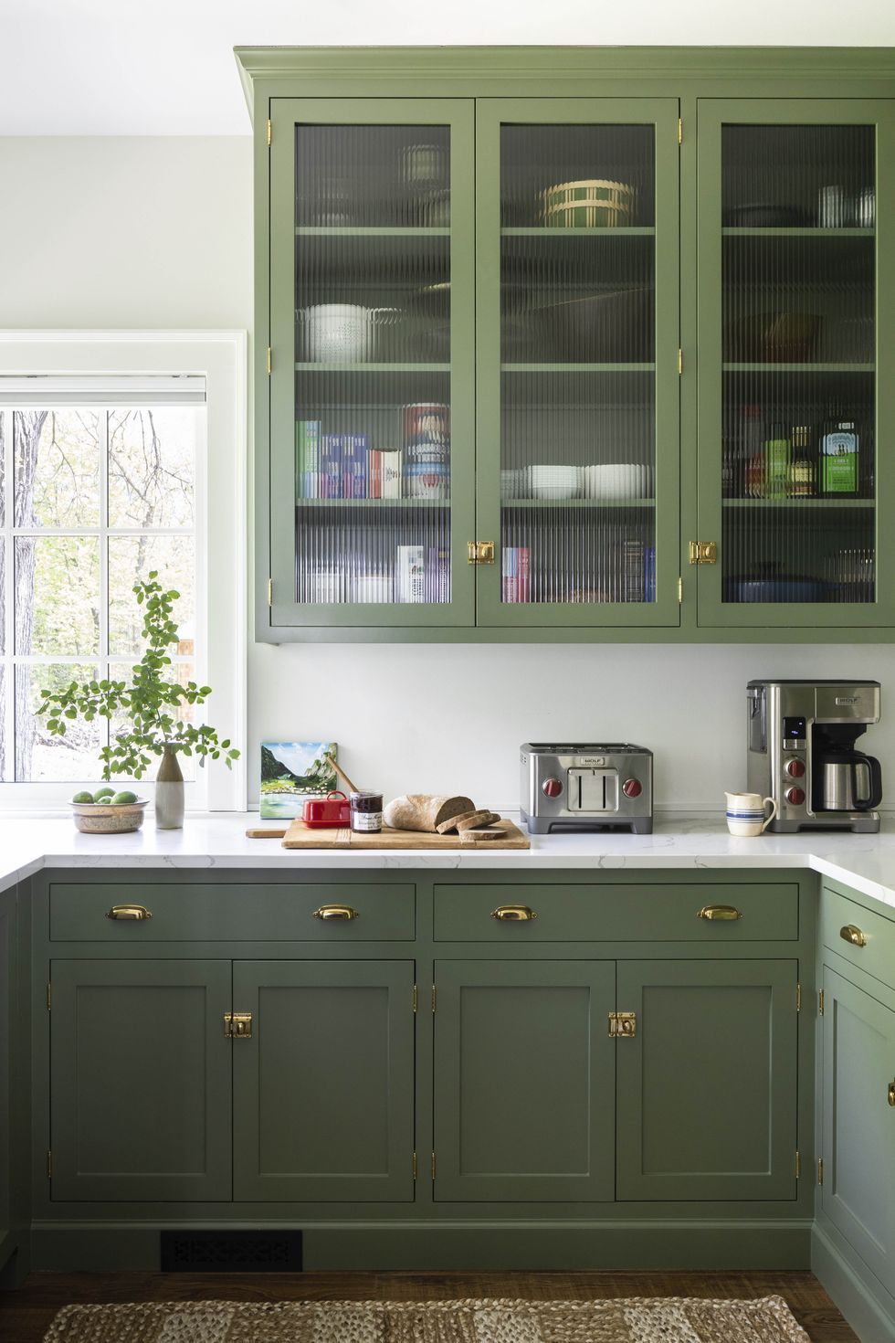green kitchen cabinets with ribbed glass upper cabinet windows, there is a board with jam and bread on the counter