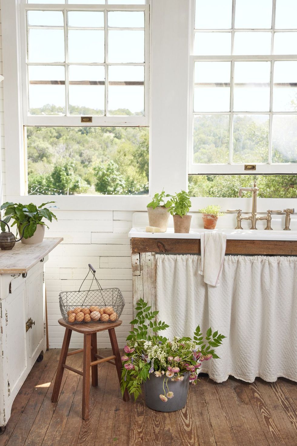 rustic white kitchen with skirted cabinetry, wooden stool with eggs in a metal basket, metal bucket of flowers, designed by claire zinnecker