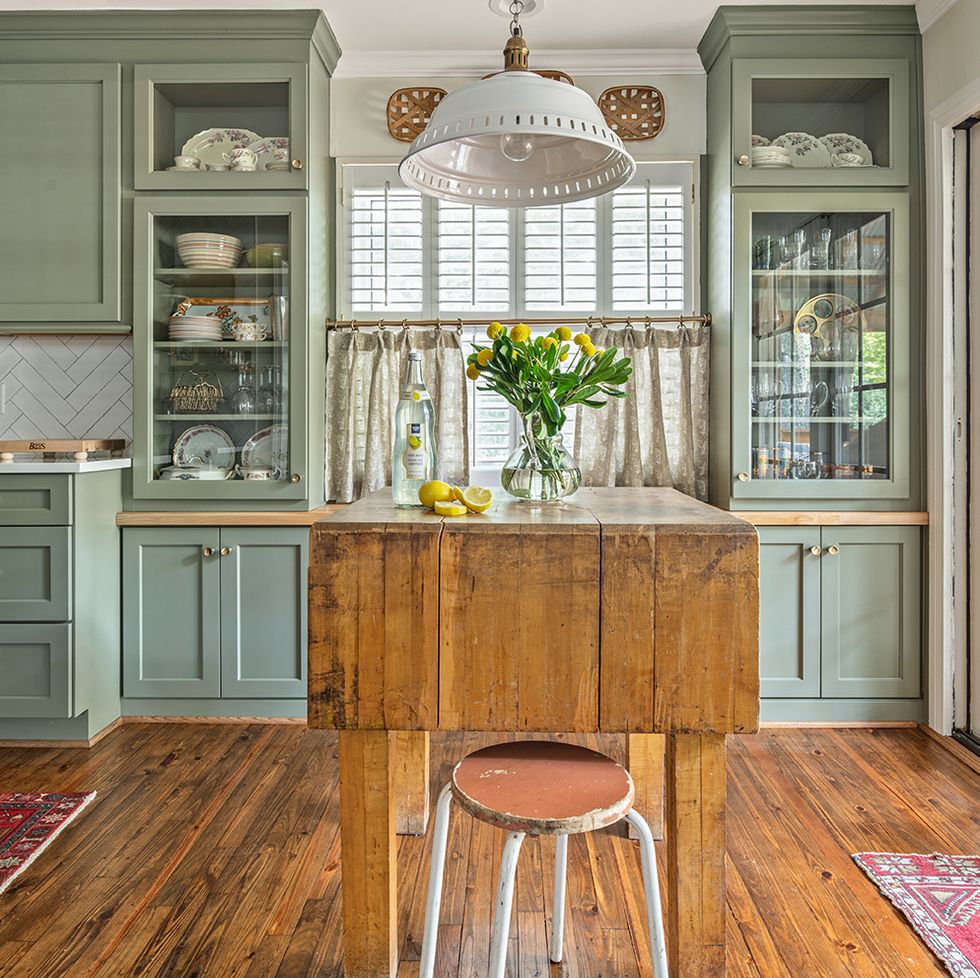 a kitchen with green cabinets with an antique butcher block table