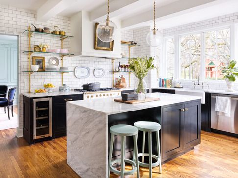 a kitchen with black cabinets and white subway tile and an island in the middle that has a waterfall style marble countertop