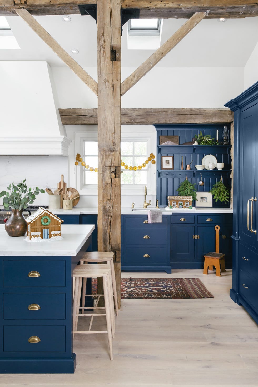 Large dark blue kitchen island with drawers, gold-tone drawer pulls, white counters, and blond wooden stools