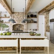 kitchen
symmetrical open shelving
and repetitive light
fixtures put the focus on
the jerusalem stone–clad,
chimney style range hood
pendants the urban electric
co seating verellen
paint snow white,
benjamin moore counter
coral stone island and
beams pecky cypress