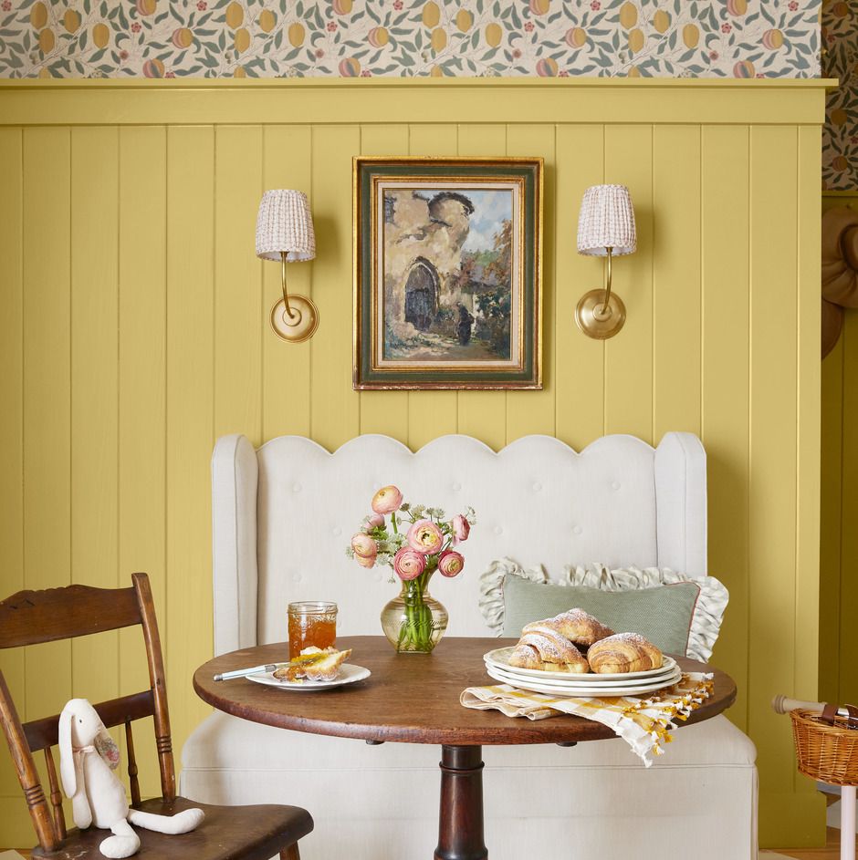 a scalloped edged settee that is white sits against yellow walls with a round wood table