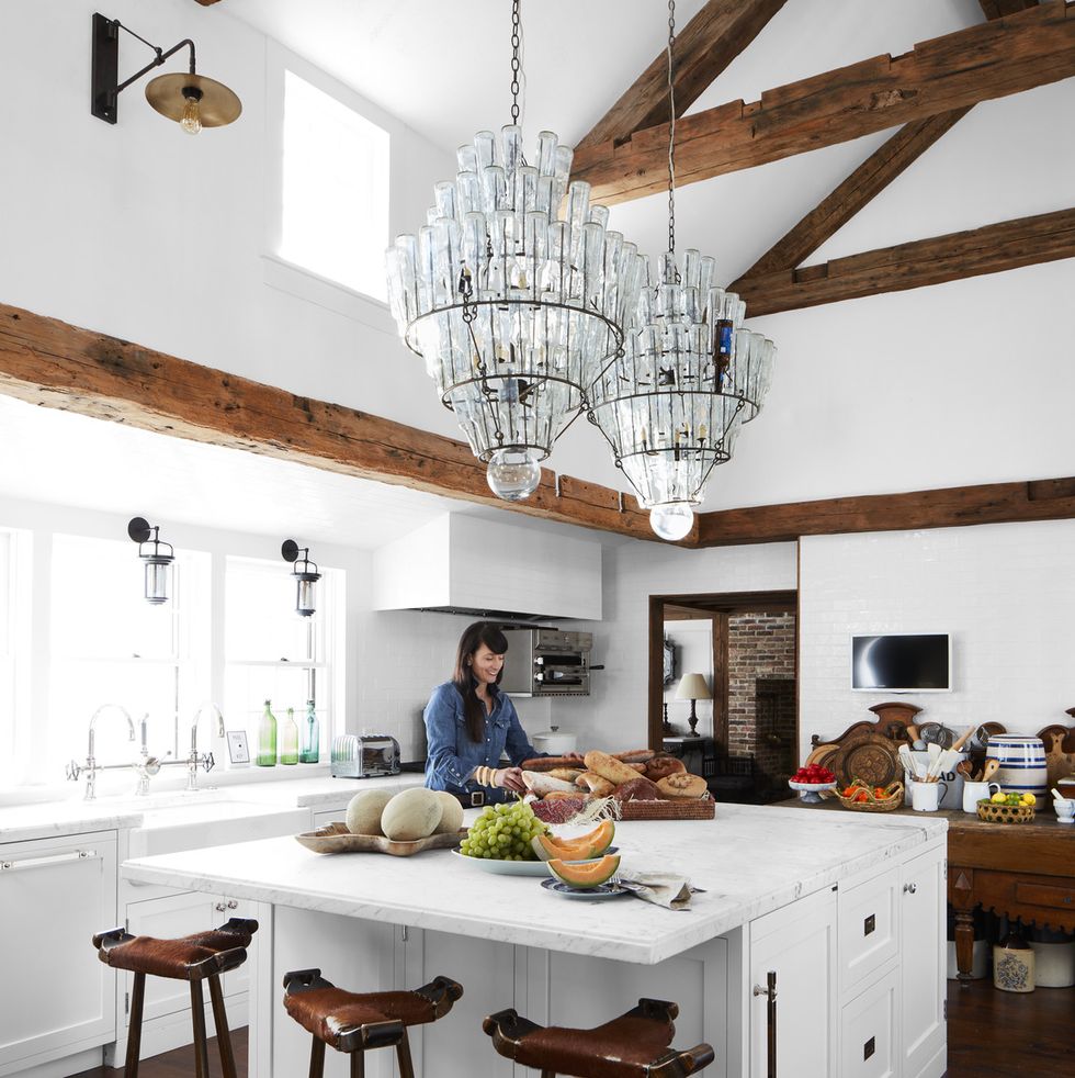 a while kitchen with wood ceiling beam and two massive crystal chandeliers over the island