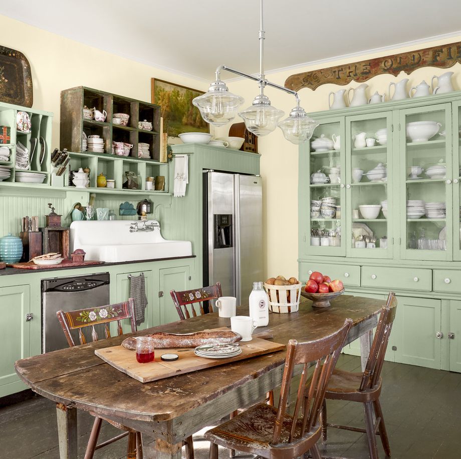 a mint green and off white kitchen has a table in the middle made of wood and a clear glass light fixture hanging above
