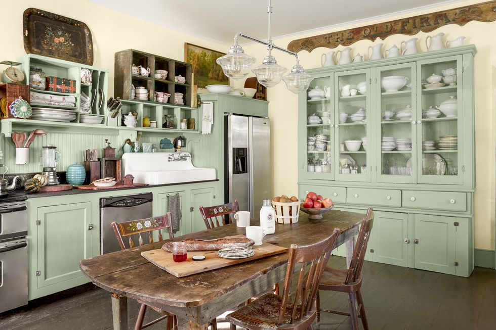 a kitchen with mint green painted cabinets and a collection of white dishes and a table in the middle