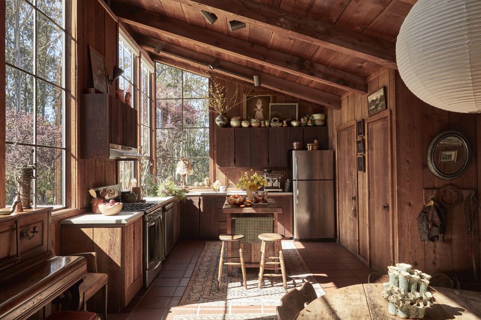 a kitchen made mostly of wood with a small island in the middle and a big window on the left