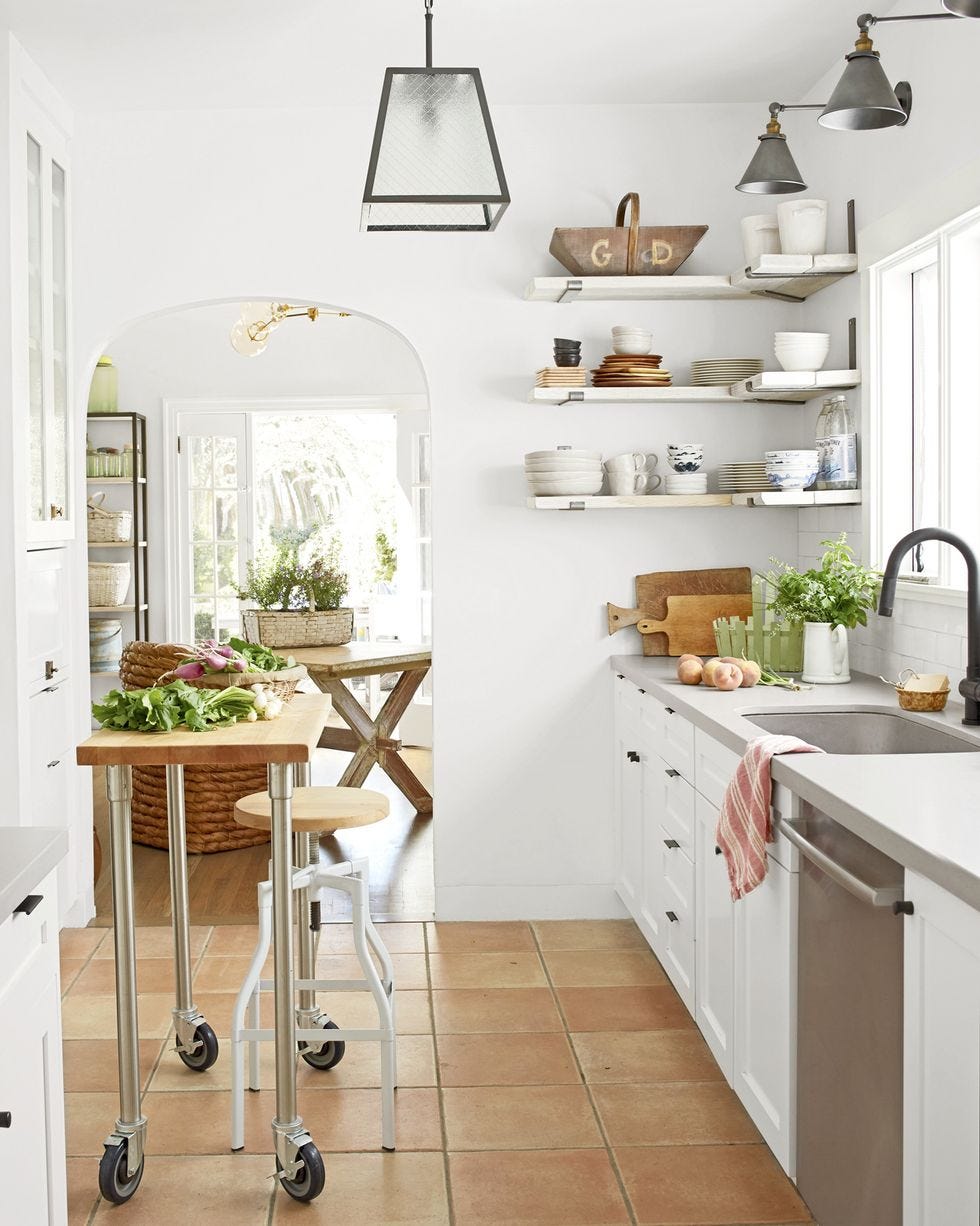 a small galley style kitchen with white cabinets and terra cotta floors