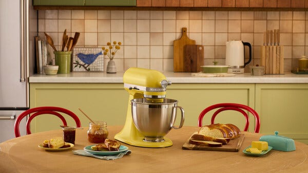 yellow stand mixer on a kitchen table with baked goods and jars of jam