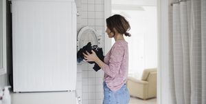 Side view of woman loading clothes in washing machine at home