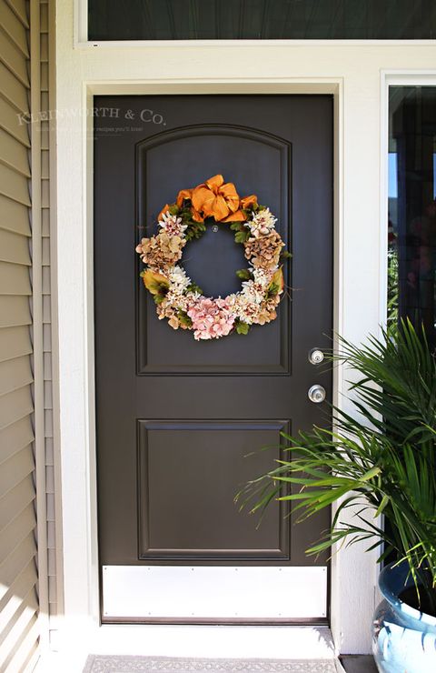 wreath with silk flowers and an orange bow hanging on black door