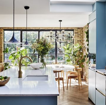 an open plan kitchen space with crittall doors, blue units, exposed brick walls, pendant lighting and a round dining table with chairs